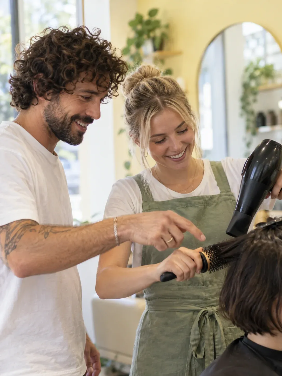 Experienced stylist coaching an apprentice through a blow-dry